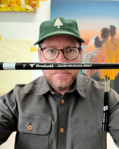 David Rice wearing glasses and a green cap, holding two Trekell brushes across and beside his face, with colorful artwork behind him.
